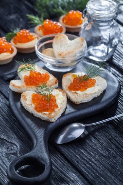 Yağ ve kırmızı havyarla servis edilen kalp şeklinde aperatifler siyah ahşap bir masada.