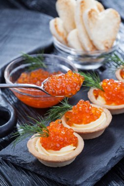 Tereyağlı tartlar, kırmızı havyar ve siyah ahşap bir masada dereotlar..