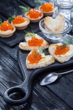 Yağ ve kırmızı havyarla servis edilen kalp şeklinde aperatifler siyah ahşap bir masada.