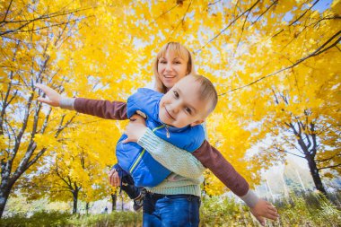 Anne ve çocuğu sarı yapraklarda eğlenin