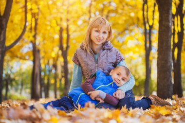 Anne ve çocuğu sarı yapraklarda eğlenin