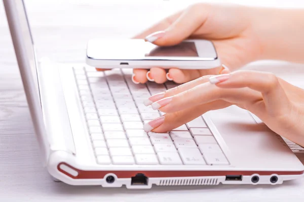 Mãos com telefone inteligente e teclado do computador — Fotografia de Stock