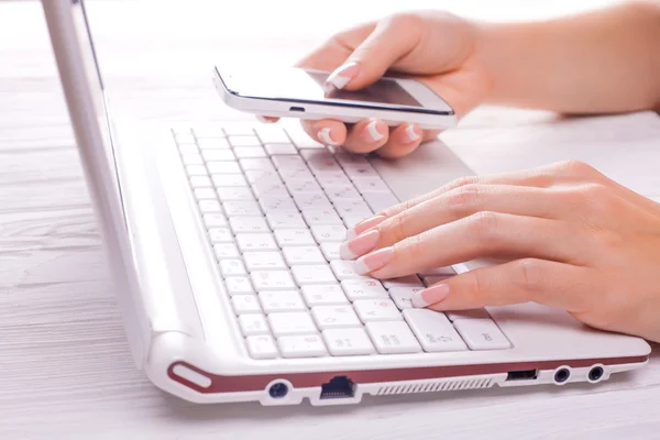 Manos con el teléfono inteligente y el teclado del ordenador — Foto de Stock