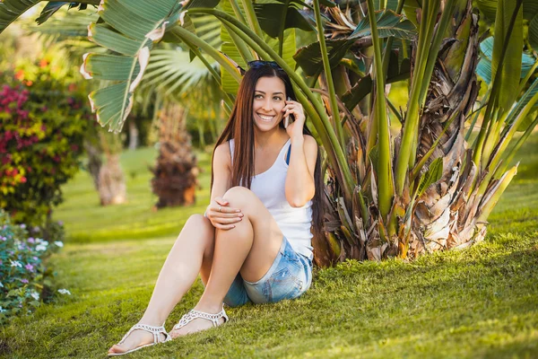 Ragazza sta parlando al telefono nel giardino delle palme — Foto Stock