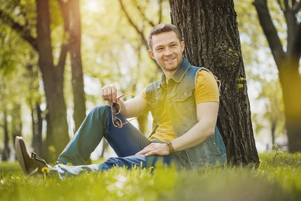 男が公園で緑の芝生に座っています。 — ストック写真