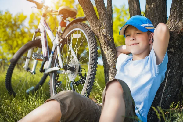 Niño feliz con una bicicleta descansando bajo un árbol — Foto de Stock