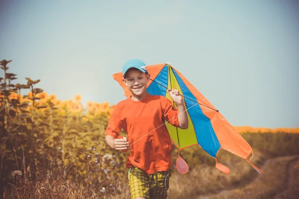 Boy running across the field with kite flying over his head — Stock Photo, Image