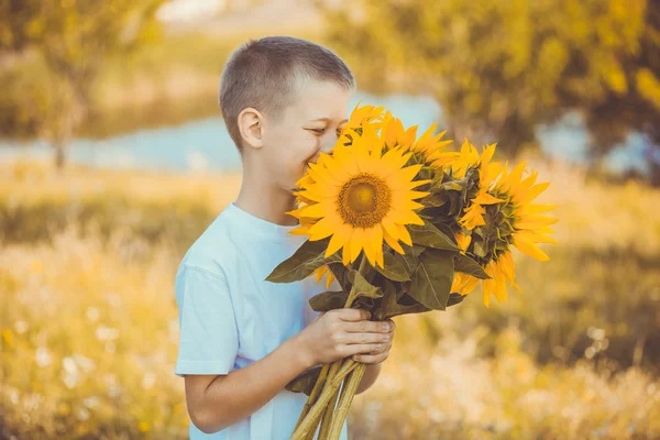 Gelukkige jongen met boeket van zonnebloemen tegen zomer veld — Stockfoto