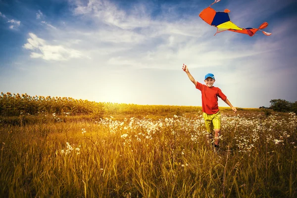 Boy running across the field with kite flying over his head — Stock Photo, Image