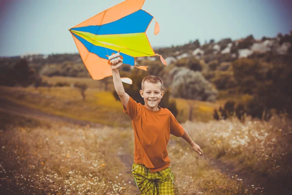 Мальчик бежит по полю с воздушным змеем над головой — стоковое фото