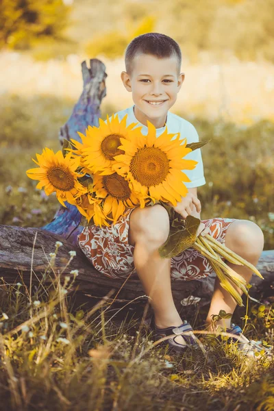 Happy boy with bouquet of sunflowers against summer field — Stock Photo, Image