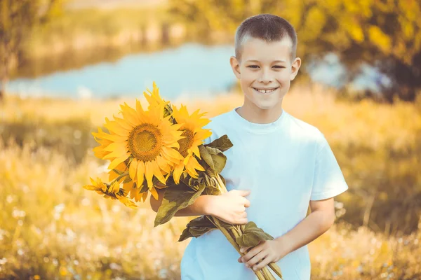 Happy boy with bouquet of sunflowers against summer field — Stock Photo, Image
