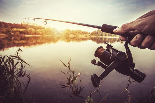 Hand med spinning och rulle på kvällen sommaren sjön — Stockfoto