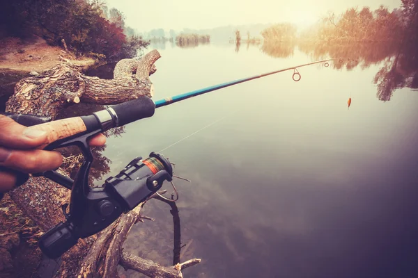 Hand with spinning and reel on the evening summer lake — Stock Photo, Image