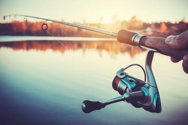 Hand with spinning and reel on the evening summer lake — Stock Photo, Image