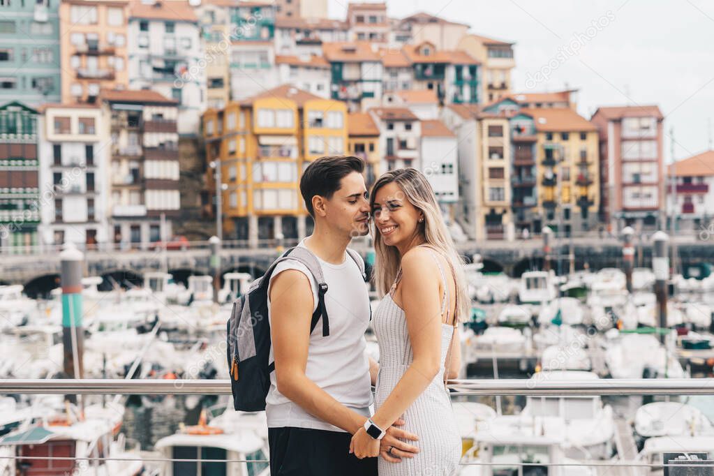 Young couple with a port and a the small village of Bermeo behind them in Vizcaya, Spain