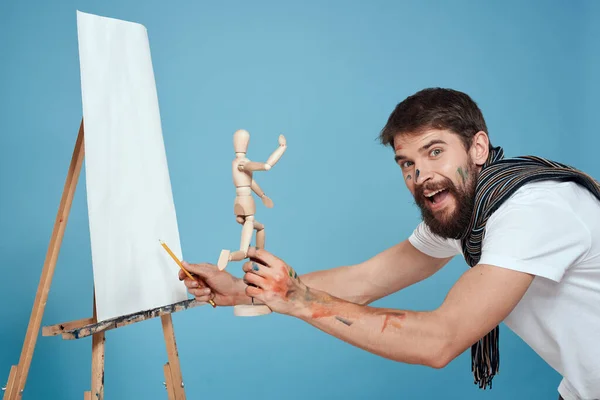 Elinde ahşap bir kukla olan erkek sanatçı yaratıcı bir hobi mavi arka plan çiziyor. — Stok fotoğraf