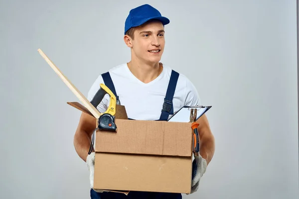 Άνθρωπος με στολή εργασίας με ένα κουτί στα χέρια του εργαλεία φορτωτή παράδοση φως φόντο — Φωτογραφία Αρχείου