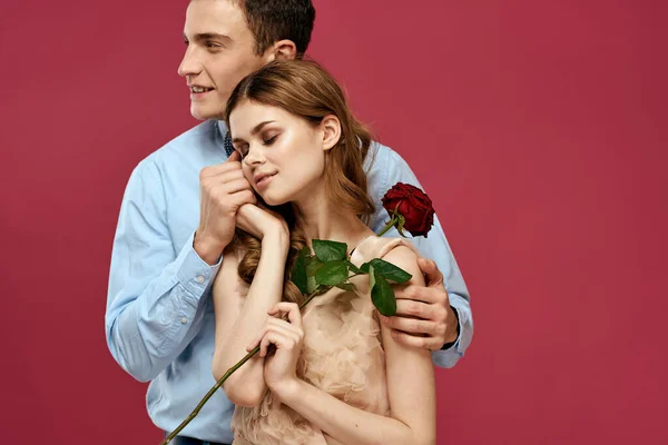 Pembe arka planda kırmızı çiçekli aşık bir adam ve kadın birbirlerine sarılırlar. — Stok fotoğraf
