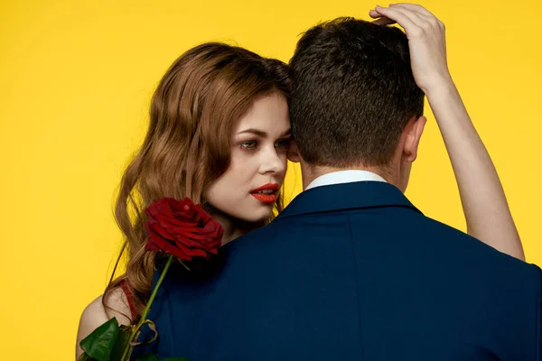Un uomo romantico abbraccia una donna in abito rosso con una rosa in mano su uno sfondo giallo — Foto Stock