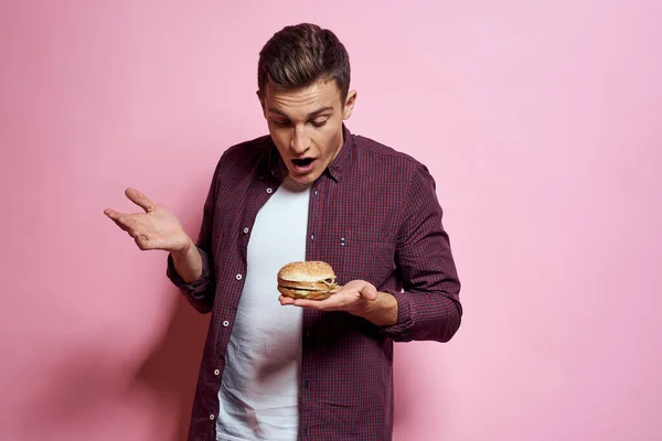 Głodny człowiek z hamburgery w rękach fast food jedzenie emocje różowy tło — Zdjęcie stockowe