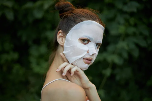 Portrait d'une femme touche son épaule avec sa main masque blanc buissons de soins de la peau en arrière-plan — Photo