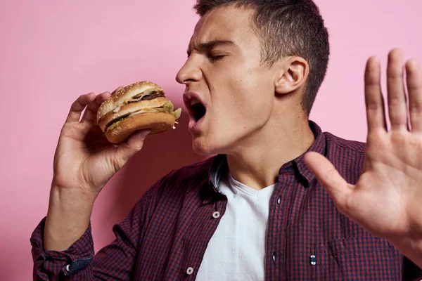 Hongerige man met hamburgers in handen fast food dieet voedsel emoties roze achtergrond — Stockfoto