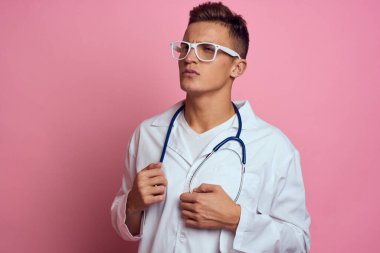 Pembe bir arka planda steteskop ve yüzünde gözlük olan tıbbi önlüklü bir erkek doktor.