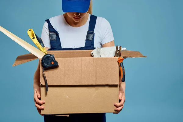 Femme de travail en uniforme avec boîte dans les mains outils chargement livraison service fond bleu — Photo