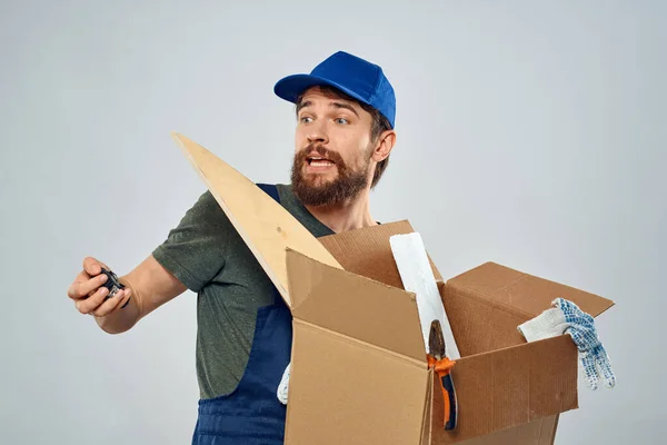 Muž v pracovní uniformě s krabicí v ruce nástroje životní styl světlo pozadí — Stock fotografie