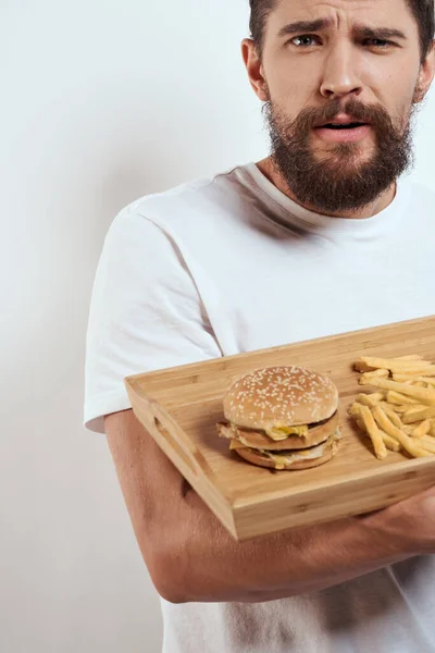 Hombre con bandeja de madera patatas fritas y hamburguesas de comida rápida modelo de calorías camiseta blanca — Foto de Stock