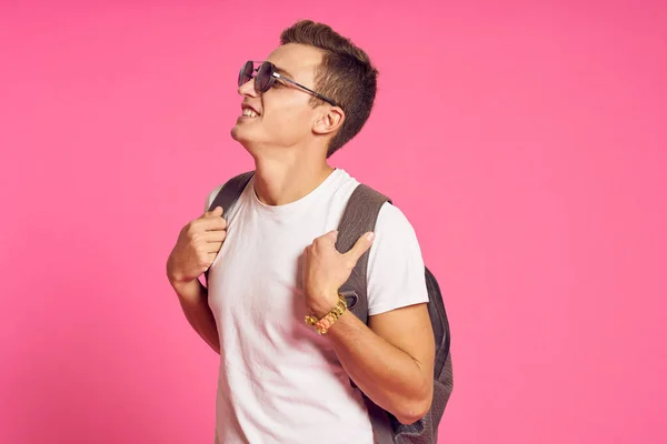 Man i solglasögon med en ryggsäck vit t-shirt ungdom stil rosa bakgrund — Stockfoto