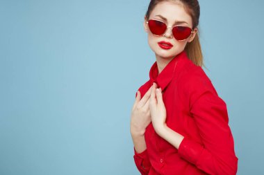 Mavi arka plandaki kırmızı gömlekli kadın yüz ve güneş gözlüklü kırmızı dudak makyajı modeli ile el ele tutuşuyor.