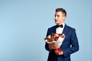Bir buket çiçekli ve mavi arka planda papyonlu romantik bir adam.