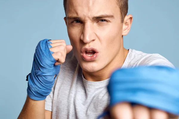 Sportovní muž v modrých boxerských rukavicích a tričku na modrém pozadí cvičení údery oříznutý pohled — Stock fotografie