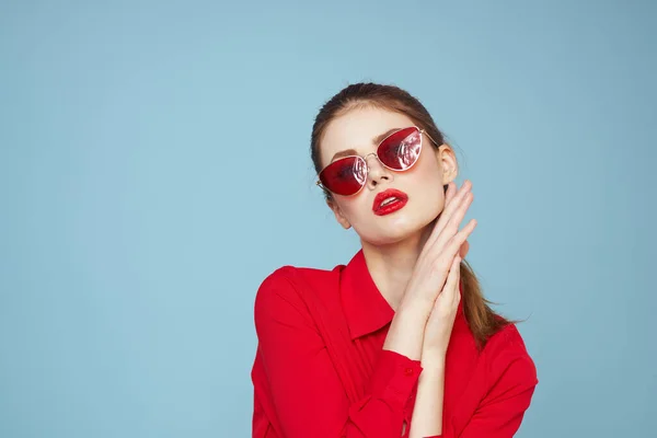 Femme en chemise rouge sur fond bleu tient les mains près du visage et lunettes de soleil rouge lèvres modèle de maquillage — Photo