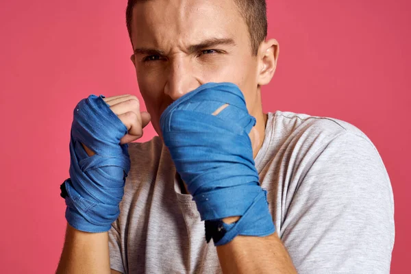 Homme sportif en gants de boxe bleus et un T-shirt sur un fond rose pratiquant des coups de poing vue recadrée — Photo