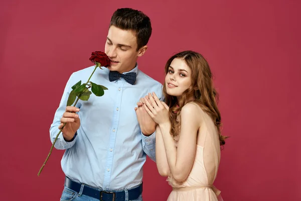Pembe arka planda kırmızı çiçekli aşık bir adam ve kadın birbirlerine sarılırlar. — Stok fotoğraf