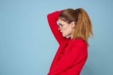 Mavi arka plandaki kırmızı gömlekli kadın yüz ve güneş gözlüklü kırmızı dudak makyajı modeli ile el ele tutuşuyor.