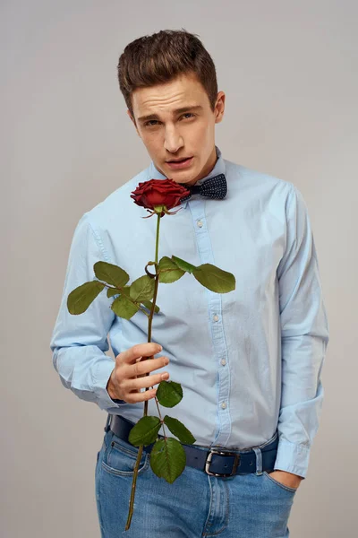 Hombre romántico con una rosa roja y una camisa azul con una pajarita alrededor de su cuello fondo gris — Foto de Stock