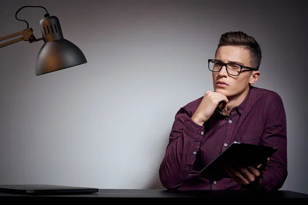 Affärsman med glasögon och en skjorta sitter vid ett bord i ett mörkt rum med en lampa beskuren utsikt — Stockfoto