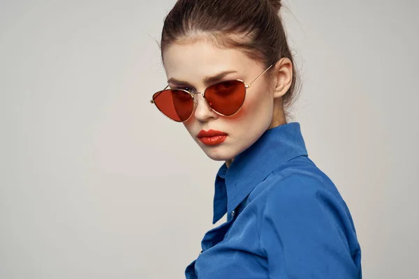 Модная женщина в солнцезащитных очках и синей рубашке, жестикулирующая руками на светлом фоне — стоковое фото
