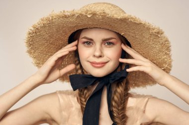 Siyah kurdeleli, saman şapkalı ve bej arka planda kırpılmış manzaralı şirin bir kız.