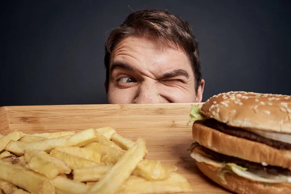 Ahşap paletli duygusal adam fast food hamburger patates kızartması yemek yaşam tarzı karanlık arka plan yiyor. — Stok fotoğraf