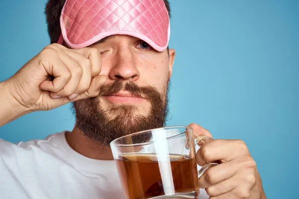 얼굴에 핑크 수면 마스크를 쓴 남자와 손에 들고 있는 차 한 잔은 하늘색 배경을 클로즈업 한 것으로 보인다 — 스톡 사진