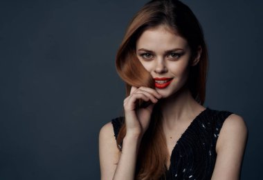 Kırmızı saçlı, gece makyajlı, siyah elbiseli hoş bayan. Arka planı gri.