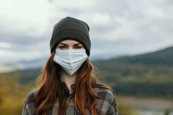 Kobieta w masce medycznej i kapelusz w górach na łonie natury jesienią — Zdjęcie stockowe