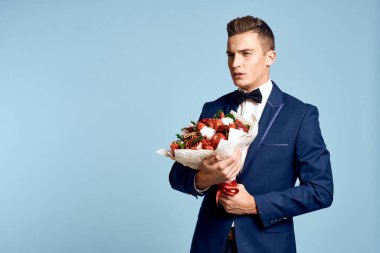 Bir buket çiçekli ve mavi arka planda papyonlu romantik bir adam.