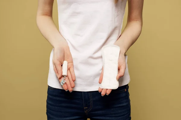 Chica con un tampón y una almohadilla en la mano sobre un fondo beige recortado vista de la menstruación días críticos —  Fotos de Stock