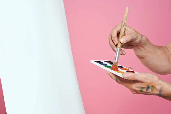손에 물감과 붓을 든 미술가가 취미적 핑크 색 배경을 그리고 있다 — 스톡 사진